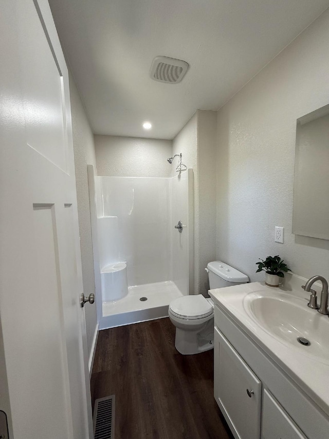 bathroom with toilet, visible vents, wood finished floors, a shower stall, and vanity
