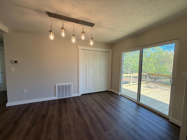 unfurnished dining area featuring baseboards, dark wood-type flooring, visible vents, and a textured ceiling