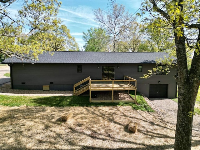 back of house with roof with shingles, driveway, an attached garage, a deck, and crawl space