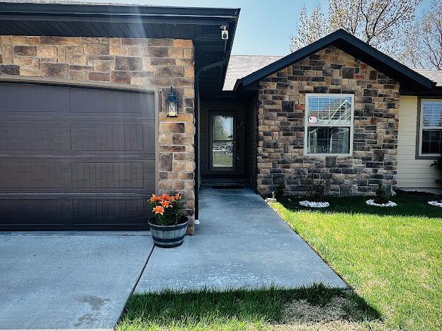 view of exterior entry with stone siding, a lawn, and a garage