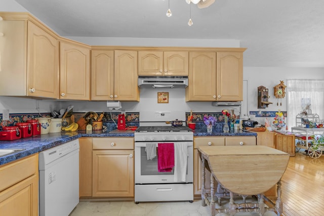 kitchen featuring dark countertops, under cabinet range hood, white appliances, and light brown cabinetry