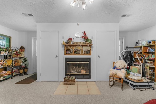 interior space featuring carpet floors, a textured ceiling, visible vents, and a glass covered fireplace