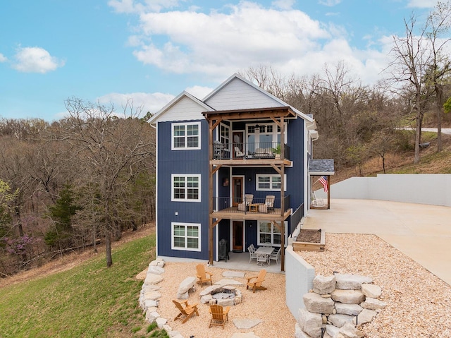 back of house featuring concrete driveway, a patio area, a balcony, and an outdoor fire pit