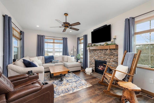 living area with dark wood-style floors, a ceiling fan, a stone fireplace, visible vents, and recessed lighting