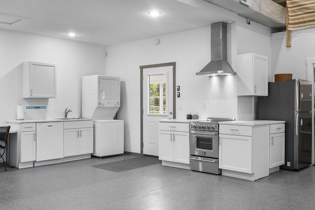kitchen featuring stacked washer / drying machine, white cabinets, stainless steel appliances, wall chimney range hood, and a sink