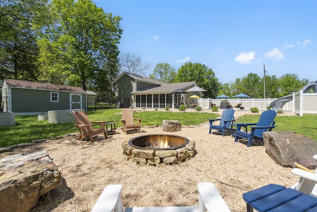 view of yard featuring a fenced backyard, an outdoor fire pit, an outdoor structure, and a sunroom