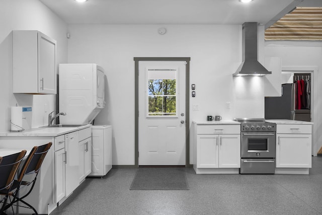 kitchen with a sink, stacked washer and clothes dryer, wall chimney range hood, light countertops, and appliances with stainless steel finishes