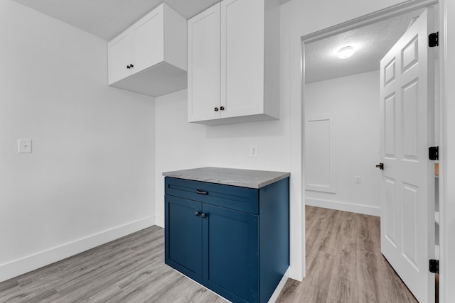 kitchen featuring light wood-style flooring, baseboards, blue cabinetry, and white cabinets