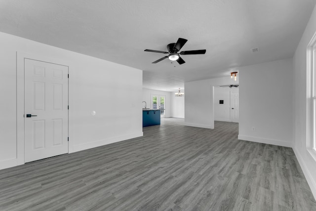 unfurnished living room featuring ceiling fan with notable chandelier, baseboards, and wood finished floors
