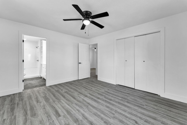 unfurnished bedroom featuring a closet, ensuite bathroom, wood finished floors, and baseboards