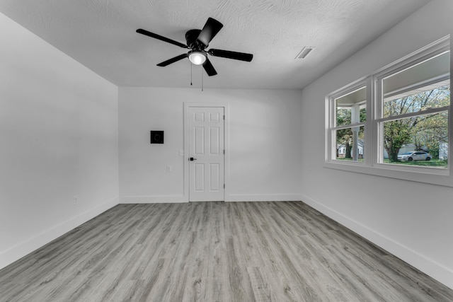 empty room featuring baseboards, a ceiling fan, visible vents, and light wood-style floors