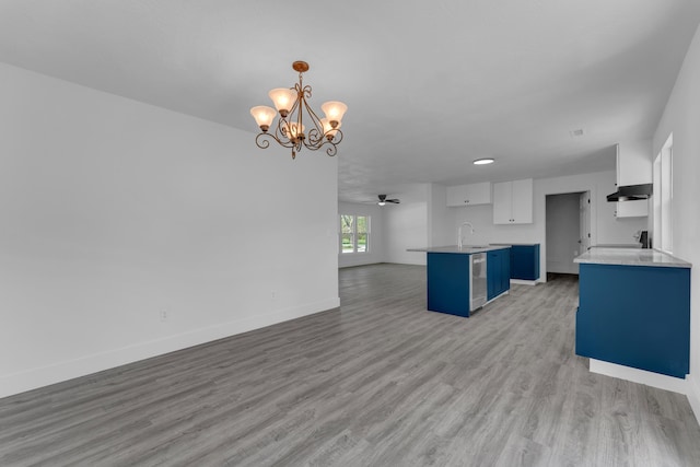 kitchen with a sink, open floor plan, baseboards, under cabinet range hood, and light wood-style floors