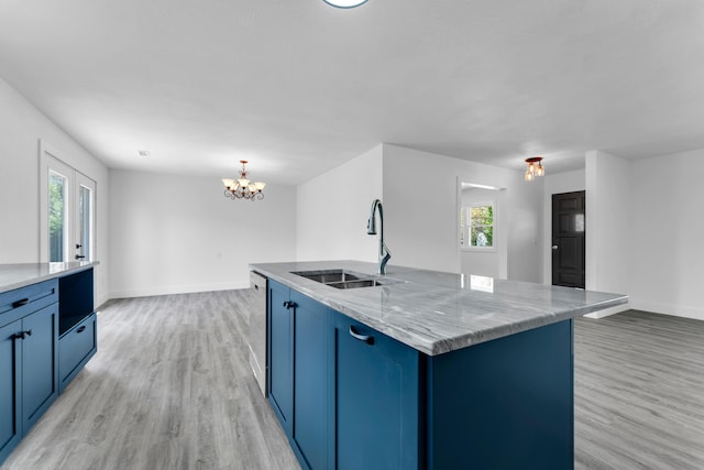 kitchen featuring light wood-style flooring, an island with sink, a sink, baseboards, and light stone counters