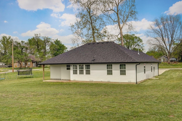 rear view of property featuring a lawn, roof with shingles, and a trampoline