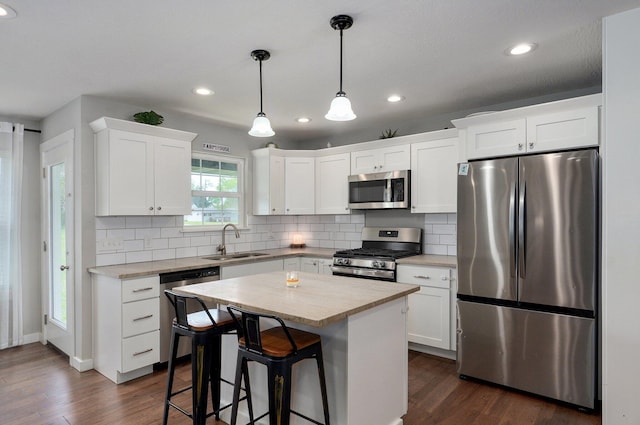 kitchen with stainless steel appliances, light countertops, a sink, tasteful backsplash, and dark wood-style flooring