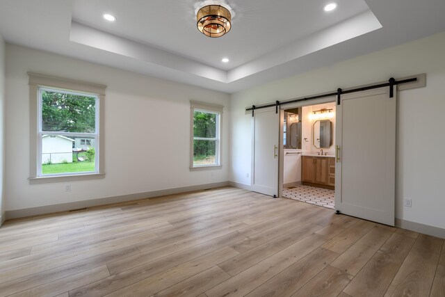 3800 W Broadmoor St, Springfield, MO 65807 - unfurnished bedroom with a barn door, a tray ceiling, light wood-style flooring, recessed lighting, and ensuite bath