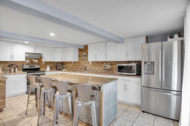 kitchen with decorative backsplash, light tile patterned floors, under cabinet range hood, appliances with stainless steel finishes, and a sink