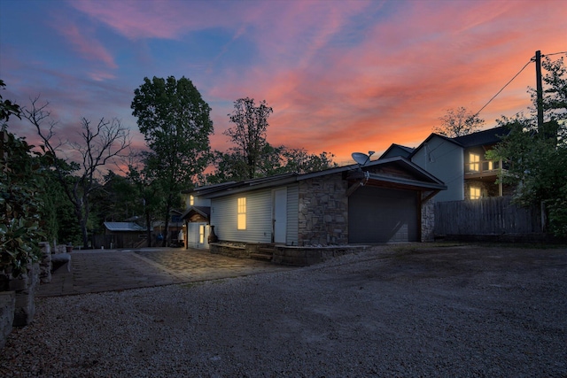 view of home's exterior with stone siding, dirt driveway, an attached garage, and fence