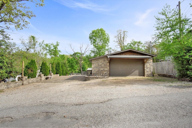 exterior space featuring a garage, driveway, stone siding, and fence