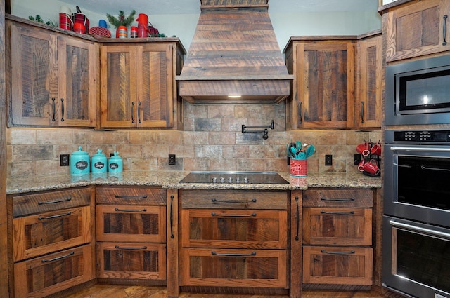 231 Cedar Stone, Ozark, MO 65721 - kitchen featuring stainless steel appliances, backsplash, light stone countertops, brown cabinetry, and premium range hood
