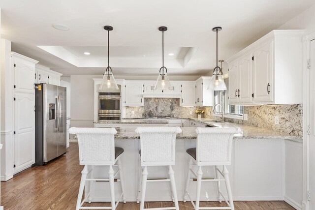 kitchen featuring a tray ceiling, decorative backsplash, a peninsula, appliances with stainless steel finishes, and white cabinetry