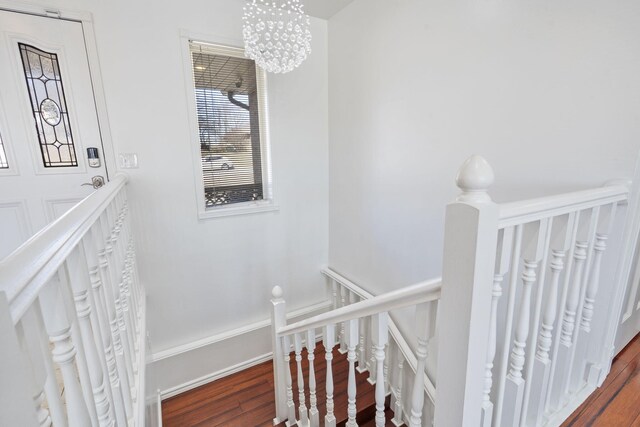 staircase featuring baseboards, wood finished floors, and a notable chandelier