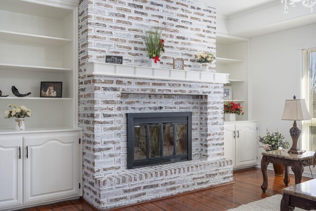 living area with dark wood-type flooring, a brick fireplace, and built in shelves