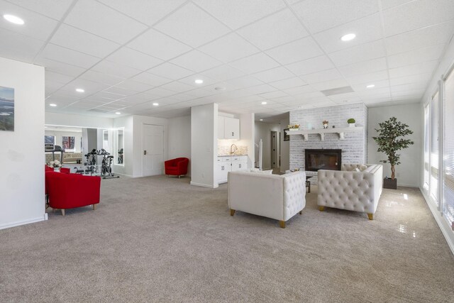 living area with a paneled ceiling, baseboards, a fireplace, and light colored carpet