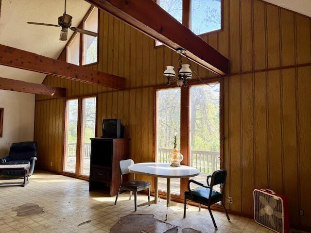 dining space with high vaulted ceiling, ceiling fan with notable chandelier, wooden walls, light floors, and beamed ceiling