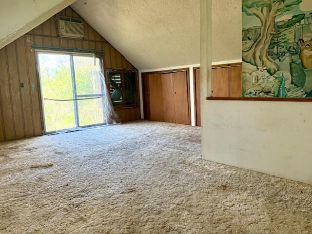 bonus room featuring wood walls, a textured ceiling, lofted ceiling, carpet flooring, and a wall unit AC