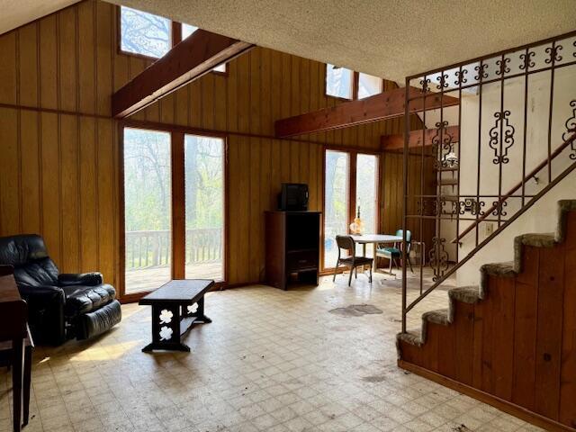 living area featuring lofted ceiling, tile patterned floors, wood walls, and stairs