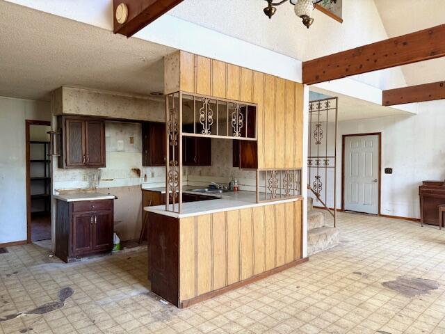 kitchen with tasteful backsplash, light floors, an inviting chandelier, beamed ceiling, and baseboards