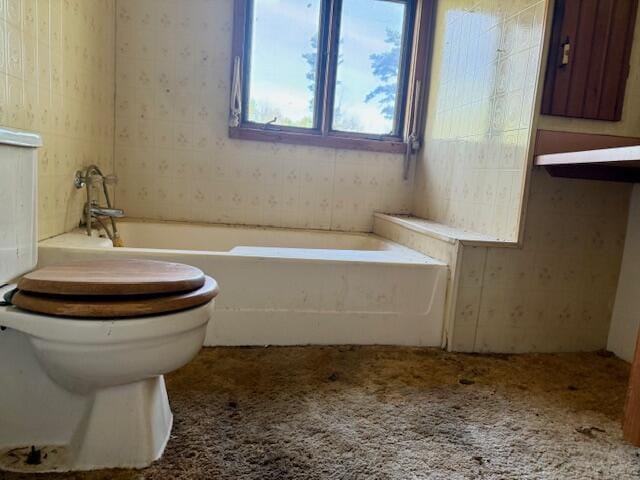 bathroom with a garden tub, toilet, and wallpapered walls