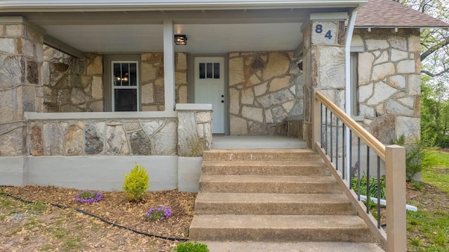 entrance to property with stone siding and a shingled roof