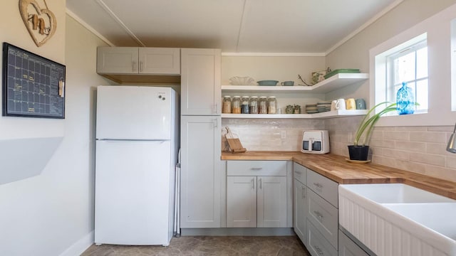 kitchen with a sink, wood counters, tasteful backsplash, crown molding, and freestanding refrigerator