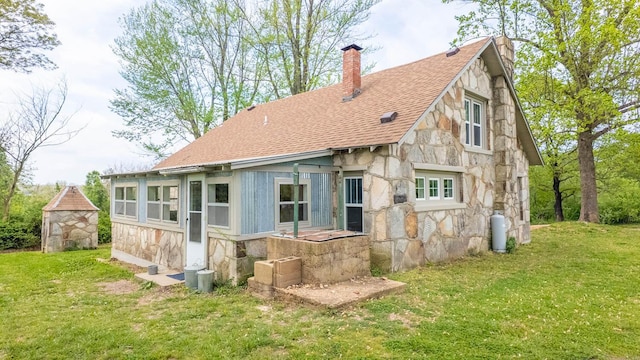 rear view of house with roof with shingles, a yard, stone siding, and a chimney