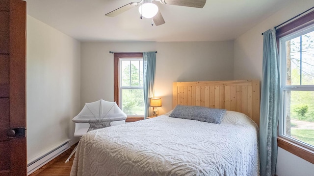 bedroom featuring wood finished floors, ceiling fan, a baseboard heating unit, and multiple windows