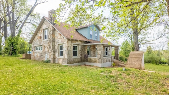 rear view of house featuring a lawn, a chimney, and stone siding