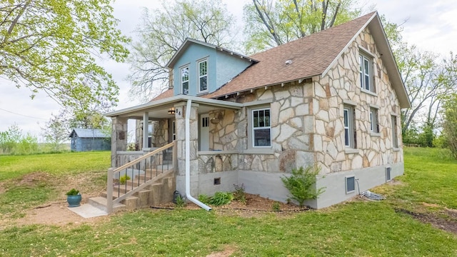 view of front of home with covered porch, a front yard, a shingled roof, and stone siding