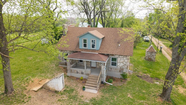 new england style home with a front lawn, covered porch, stairs, stone siding, and roof with shingles