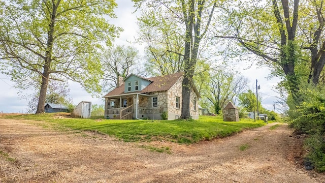 view of side of home with driveway, a yard, a porch, and stone siding
