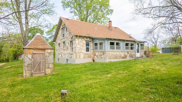 rear view of property with a chimney, a yard, a shingled roof, and stone siding