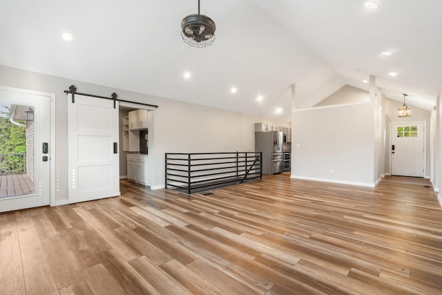 bonus room featuring light wood-style floors, a barn door, a healthy amount of sunlight, and vaulted ceiling