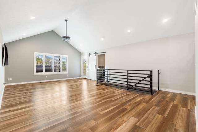 unfurnished living room with a barn door, wood finished floors, high vaulted ceiling, baseboards, and recessed lighting