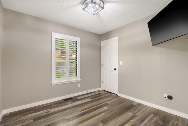 unfurnished room featuring dark wood-style flooring, baseboards, visible vents, and a textured ceiling