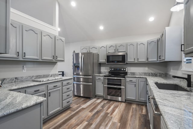 kitchen featuring gray cabinets, appliances with stainless steel finishes, light stone countertops, a sink, and lofted ceiling