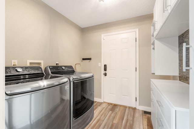 laundry room featuring baseboards, light wood-type flooring, cabinet space, and washing machine and clothes dryer