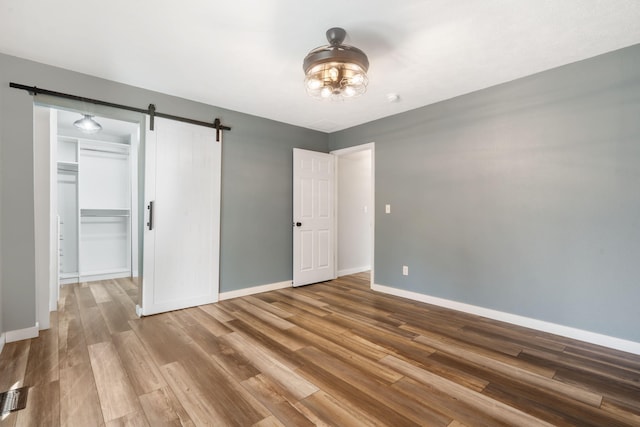 unfurnished bedroom featuring baseboards, a spacious closet, a barn door, and wood finished floors