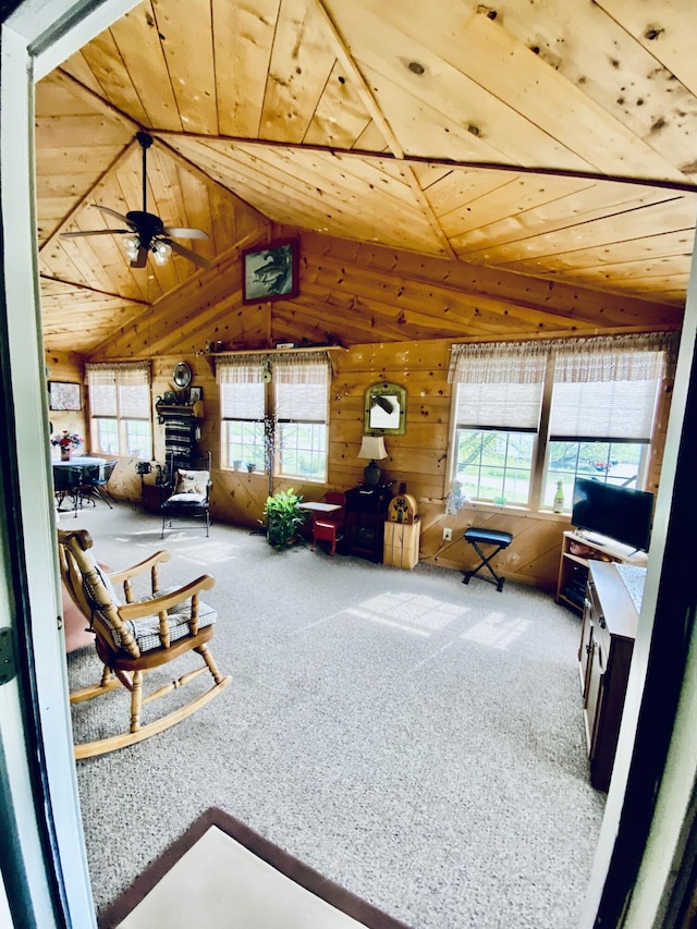 carpeted living area with wood walls, a healthy amount of sunlight, and lofted ceiling