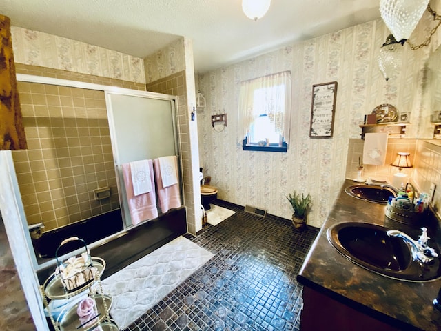 full bathroom with double vanity, a shower with door, wallpapered walls, and a sink